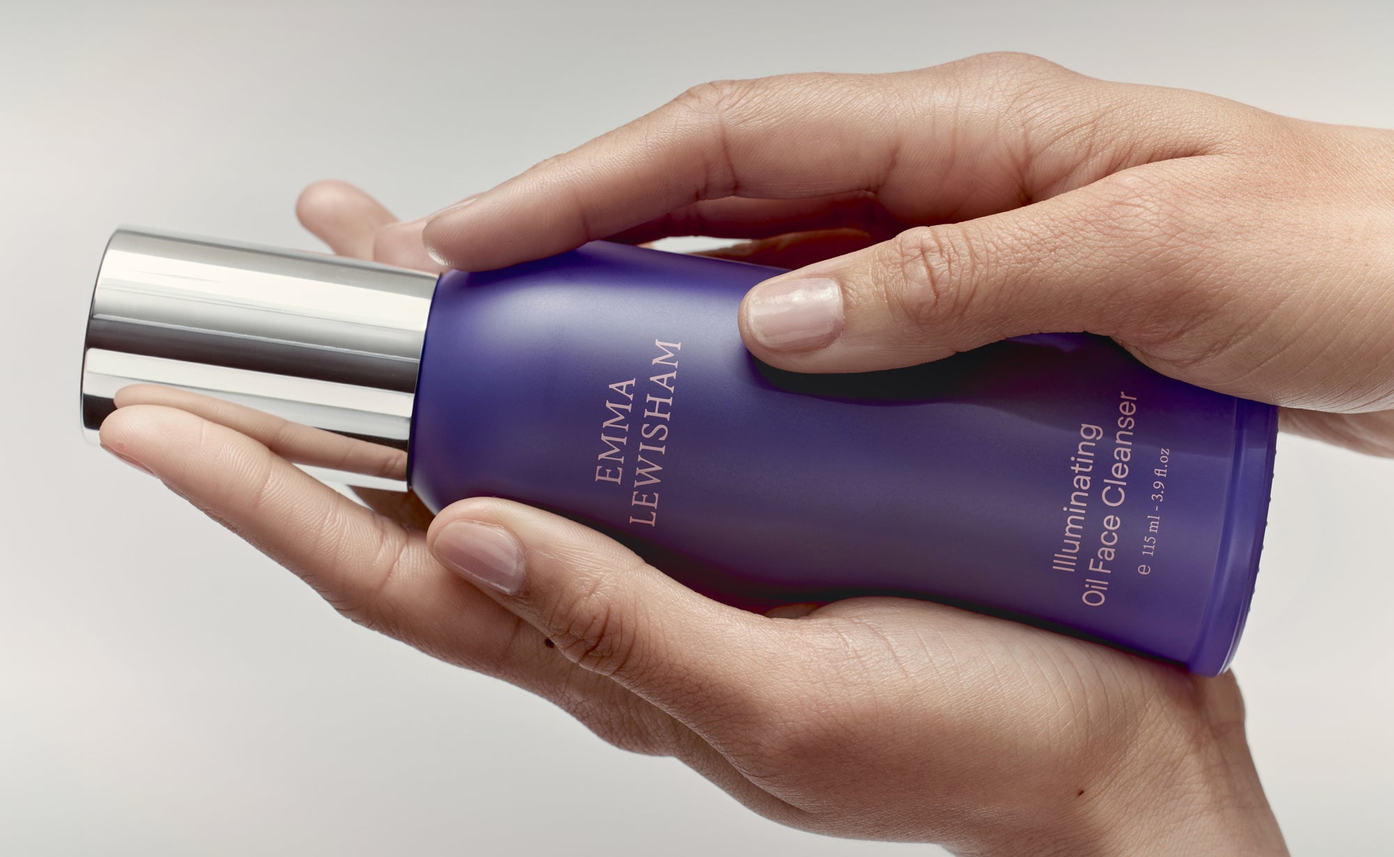 Hand holding a purple bottle with silver cap, featuring 'Emma Lewisham' branding.